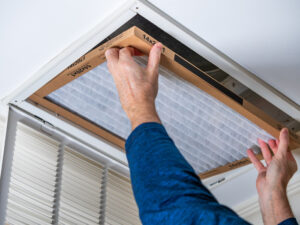 Man replacing dirty HVAC air filter in ceiling vent